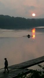 Silhouette person on lake against sky during sunset