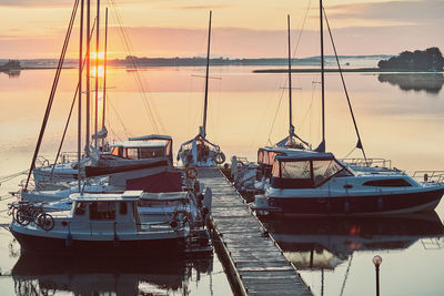 Sailboats moored at harbor against sky during sunset