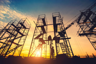 Low angle view of silhouette cranes against sky during sunset