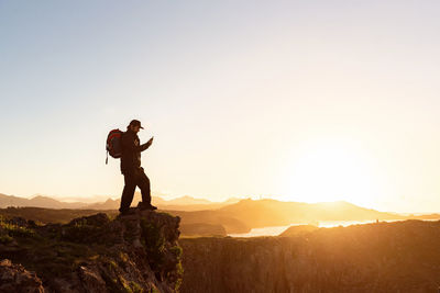 Man standing on rock against sky during sunset