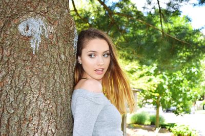 Side view of young woman standing by tree