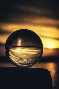 Close-up of crystal ball on water against sunset sky