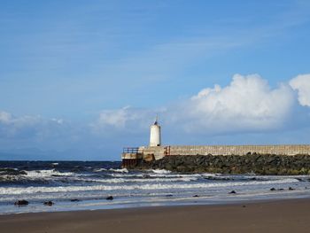 Lighthouse on beach by sea against sky