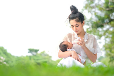 Mother feeding milk to baby girl with bottle while sitting on grass at park