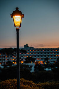 Illuminated street light and buildings against sky at dusk