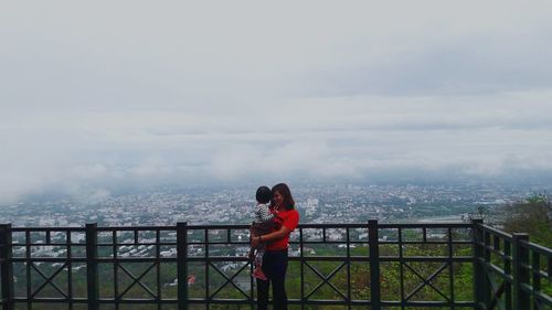 High angle view of mother carrying daughter by railing against cityscape