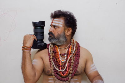 Portrait of man holding camera while standing against wall