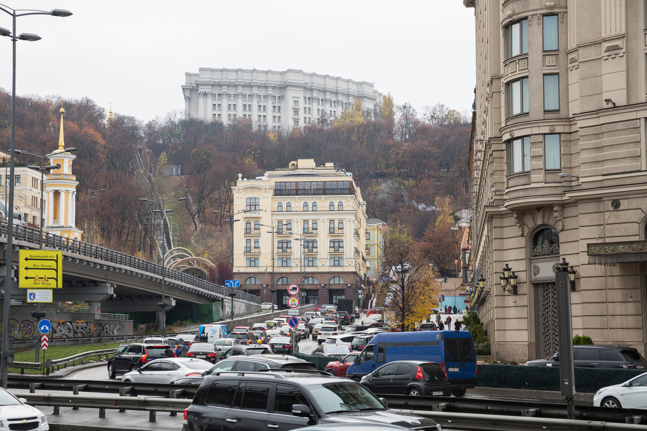 TRAFFIC ON ROAD BY BUILDINGS AGAINST SKY