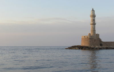 Lighthouse by sea against sky during sunset