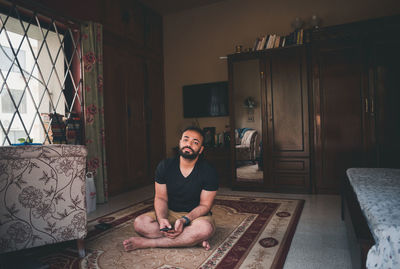 Portrait of young man sitting on carpet in living room at home