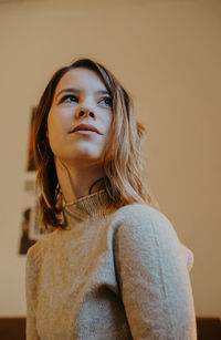 Young woman looking away against wall at home