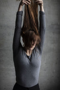 Young woman holding hair while standing against wall