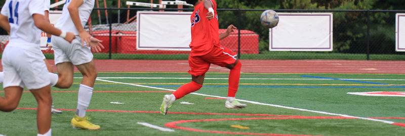 Soccer players chasing a bouncing soccer ball during a match on a turf field at a high school.