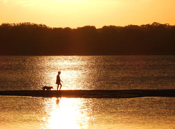 Silhouette person on sea against sky during sunset