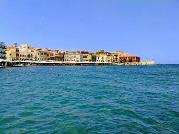 Buildings by sea against clear blue sky