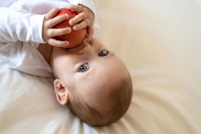 Baby lying on his back holding an apple