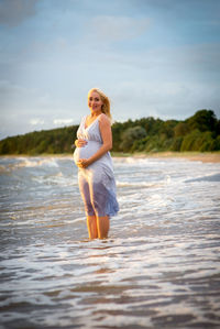 Pregnant woman standing at beach against sky