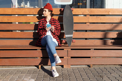 Full length of woman with skateboard sitting outdoors