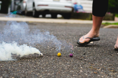 Low section of woman walking by burning fireworks on road