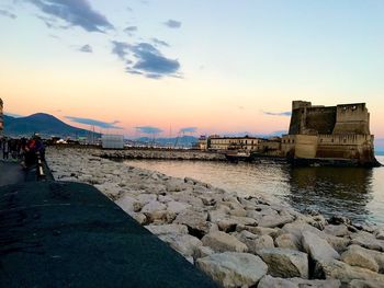 People at riverbank against sky during sunset