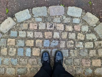 Two black shoes and legs on a cobblestone surface - top view concept.