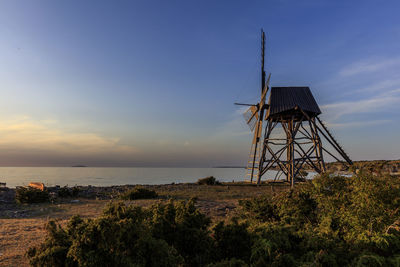 Traditional windmill by sea against sky during sunset