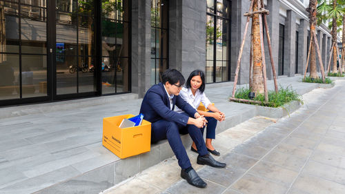 Full length of couple sitting on building in city