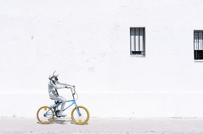 Playful boy in astronaut cycling bicycle against wall