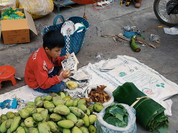 Boy reading book sitting by fruits for sale at market