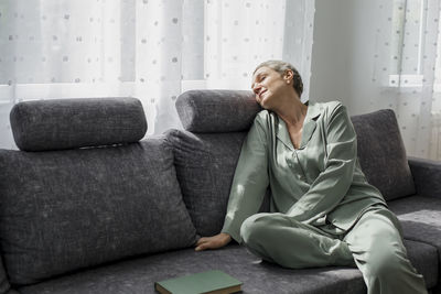 Relaxed mature woman sitting on couch in living room with closed eyes