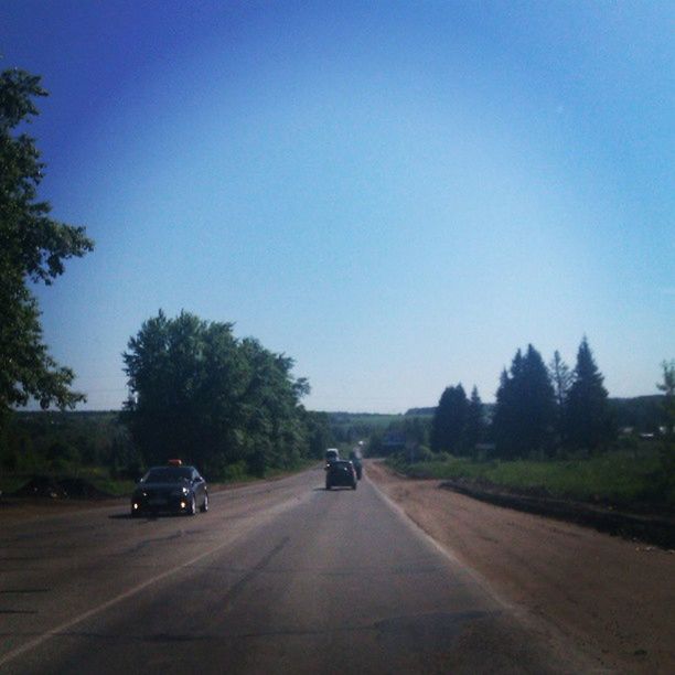 transportation, road, land vehicle, car, mode of transport, clear sky, the way forward, road marking, tree, on the move, copy space, diminishing perspective, street, blue, country road, vanishing point, travel, sky, day, outdoors