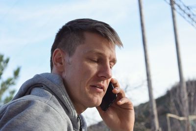 Close-up of man using mobile phone against sky