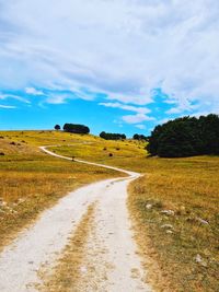 Dirt road amidst field against sky