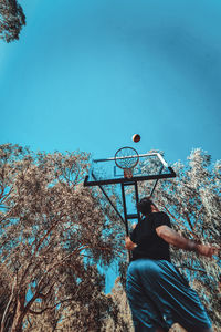 Low angle view of man putting ball in basketball hoop against clear sky