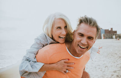 Close-up of man giving piggyback ride to happy girlfriend standing at beach