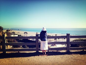 Rear view of woman standing on footbridge against sea