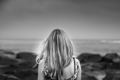 Rear view of woman standing at beach against sky