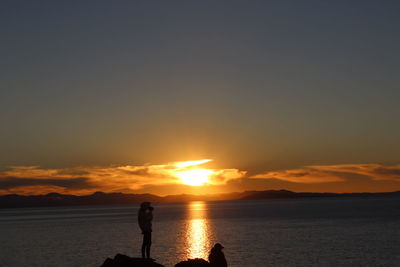 Silhouette people standing on beach against sky during sunset
