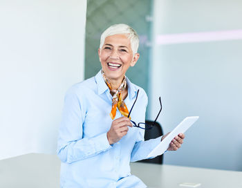 Portrait of smiling businesswoman holding digital tablet while sitting in office