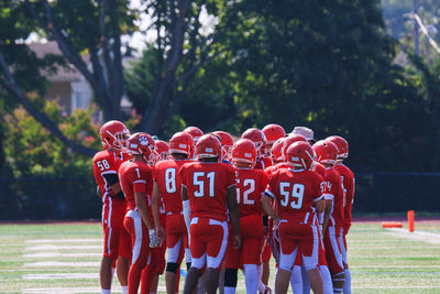 A football team in red uniforms gathers for a huddle, focused on their next play.