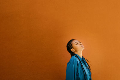 Young woman with head back standing by orange wall