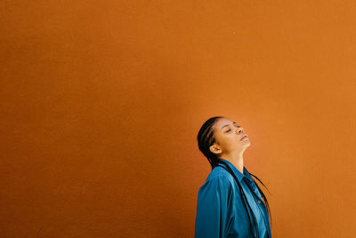 Portrait of young woman standing against yellow background