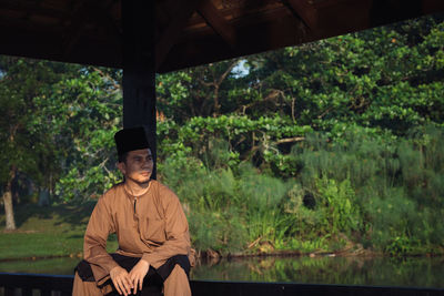 Portrait of young man sitting by plants in forest