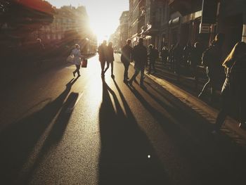 People walking on city street against bright sky