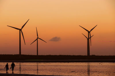View of people walking on wind farm during sunset
