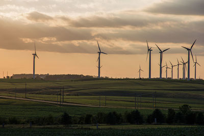 Scenic view of wind turbines on field against sky during sunset