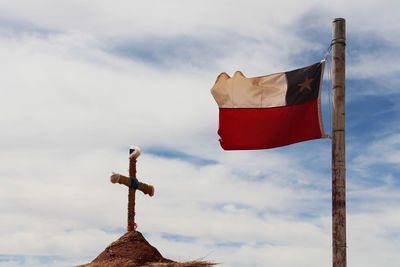 Low angle view of flag by religious cross against sky