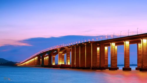 Illuminated bridge over sea against sky at sunset