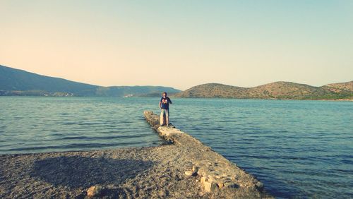 Man standing on retaining wall against sea