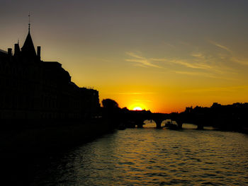 Silhouette of bridge over river against buildings during sunset